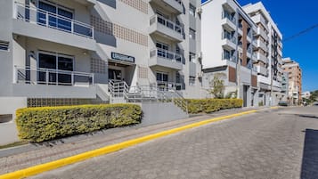 Un edificio residencial de varios pisos con balcones, cielo despejado y una acera amarilla.