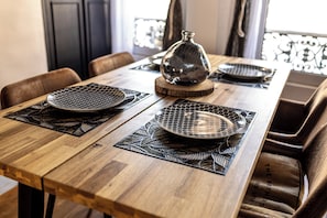 Uma mesa de jantar de madeira com jogos americanos pretos e um vaso de vidro decorativo.