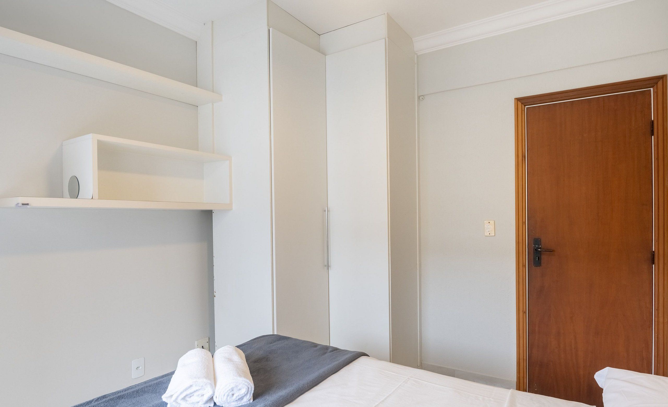 Une chambre d’hôtel avec un lit, une porte en bois et une armoire blanche.