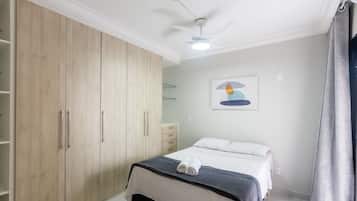 A bedroom with a bed, a wardrobe, a ceiling fan, and a painting on the wall.