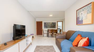 A modern living room with a flat-screen TV, a sofa, a coffee table, and a dining area in the background.