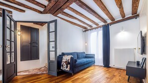 A room with wooden flooring, a blue sofa, a black cabinet, and a door with glass panels. - Triplex Belle Époque Hypercenter (Melun)