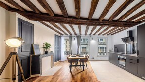A modern kitchen with wooden beams, a dining area with a table and chairs, and a view of the city through large windows. - Triplex Belle Époque Hypercenter (Melun)