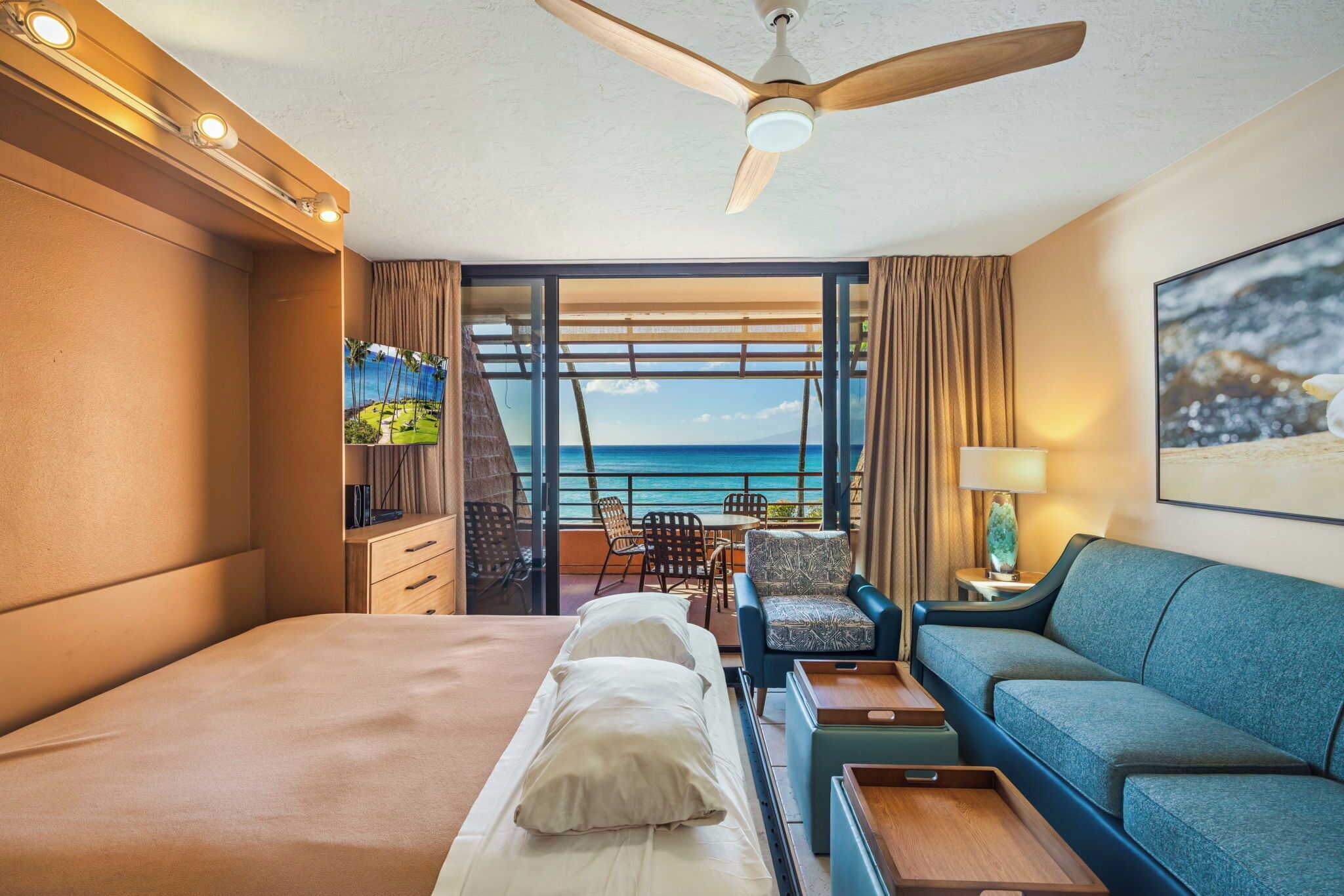 Camera d'albergo con un letto, un divano, un balcone vista mare e una ventola a soffitto.