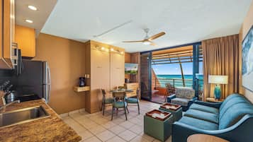 A modern hotel room with a kitchen, dining area, and a balcony with a view of the ocean.