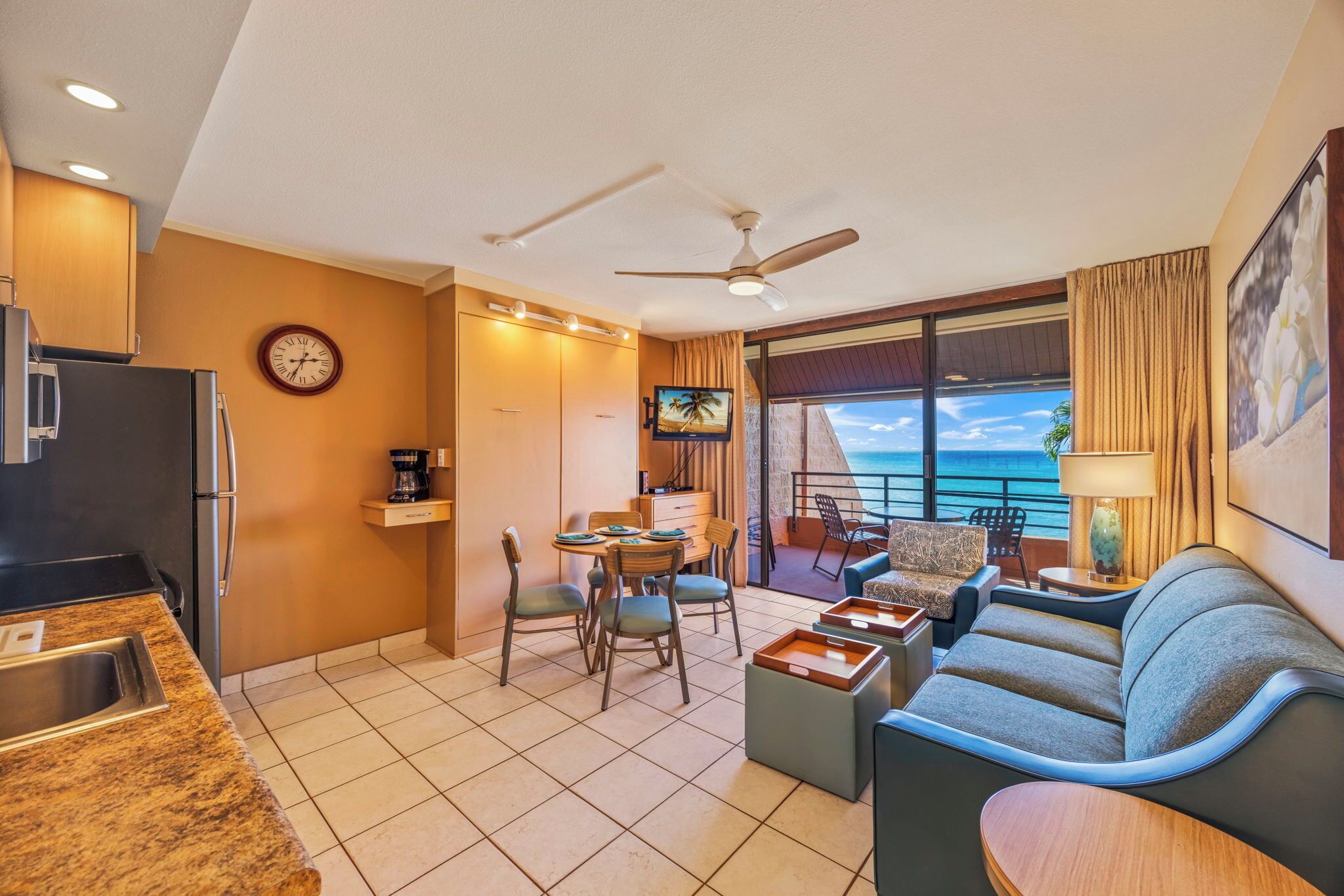 A modern hotel room with a kitchen, dining area, and a balcony with a view of the ocean.