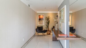 A modern reception area with a reception desk, two black chairs, a large potted plant, and framed artwork on the walls. - Apartment With Balcony 500m From the Beach Emz0504 (Guarapari)