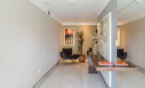 A modern reception area with a reception desk, two black chairs, a large potted plant, and framed artwork on the walls. - Apartment With Balcony 500m From the Beach Emz0504 (Guarapari)