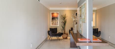 A modern reception area with a reception desk, two black chairs, a large potted plant, and framed artwork on the walls.