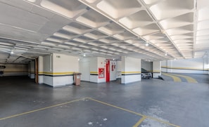 En tom parkeringskælder med højt til loftet, markerede parkeringspladser og en brandslukker.