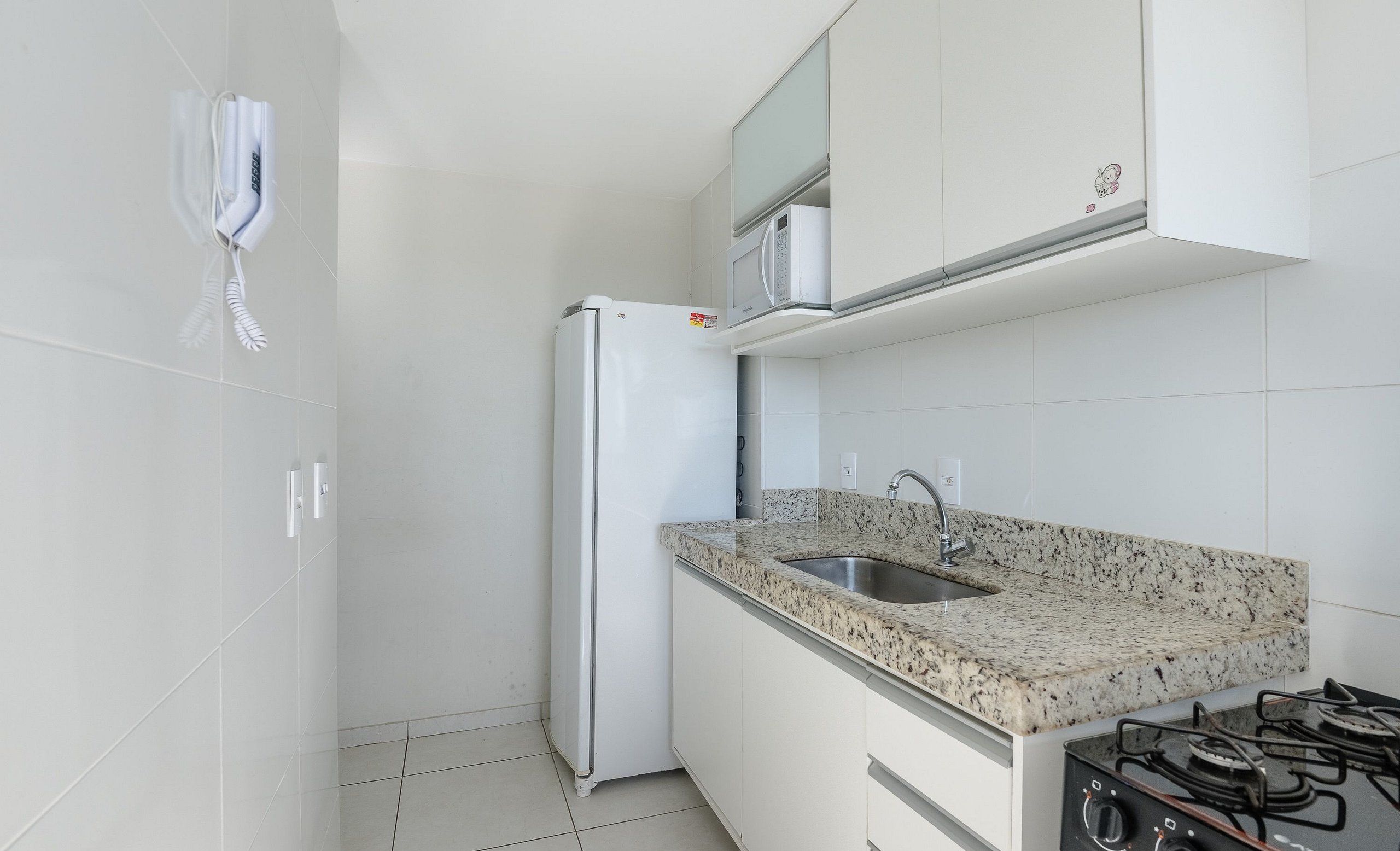 A modern kitchen with white cabinets, a granite countertop, a stainless steel sink, a built-in microwave, and a gas stove.
