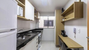 Cocina pequeña con refrigerador, doble pileta, horno y cafetera sobre una repisa de madera.
