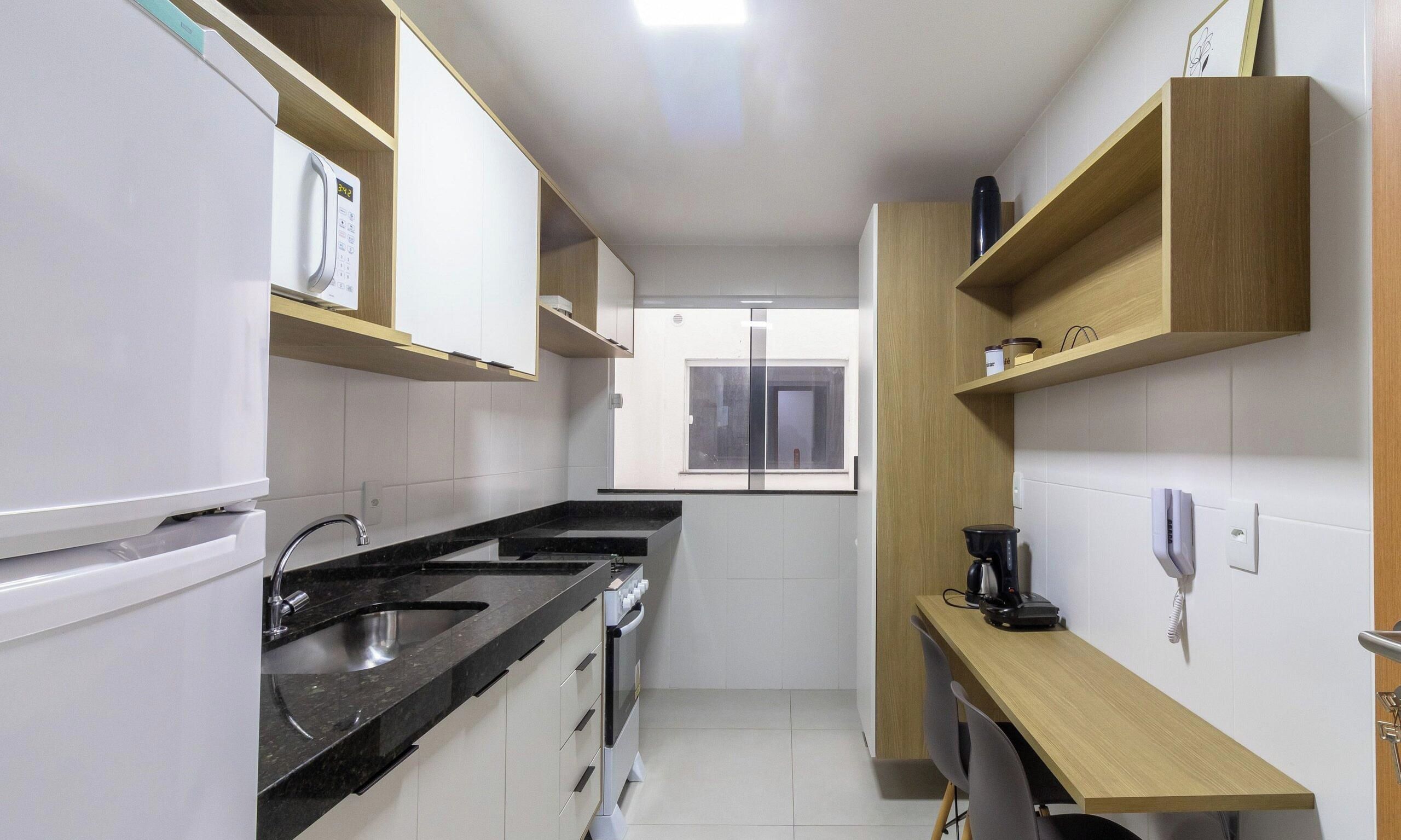Una cocina compacta con refrigerador, estufa, pileta y estantes de madera.