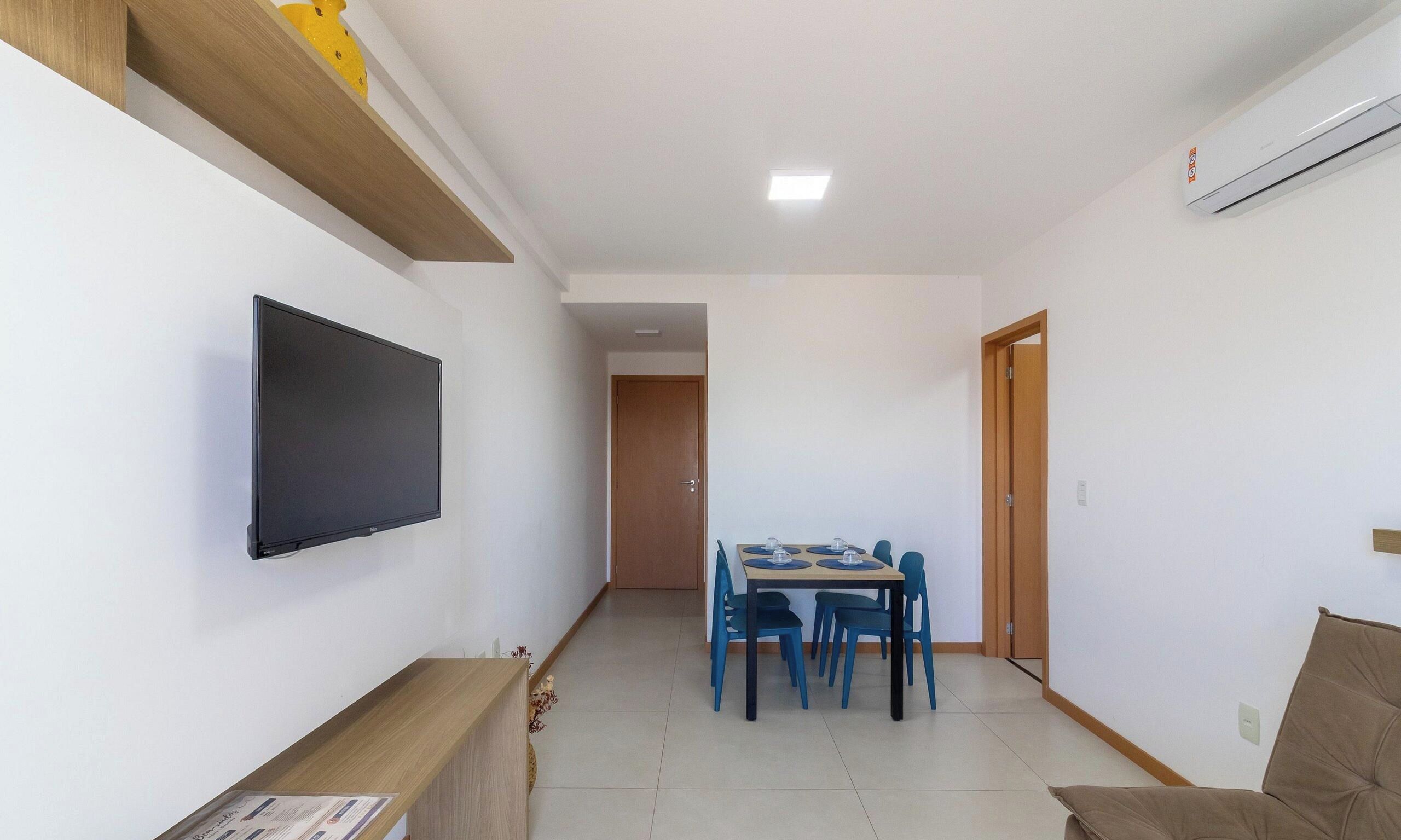 Una stanza con una TV a schermo piatto fissata al muro, un tavolo da pranzo con sedie e una porta che dà su un'altra stanza.