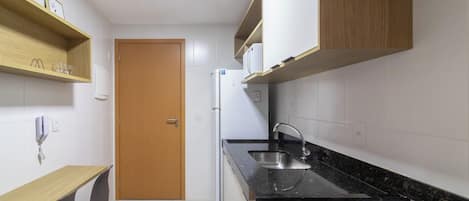 A compact kitchen with a refrigerator, a sink, and a wooden table with chairs.