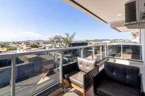 A balcony with a glass railing, two sofas, and a view of a cityscape. - Beautiful Apt Near the Beach in Cabo Frio Emt203 (Cabo Frio)