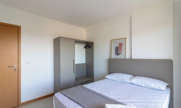 A bedroom with a bed, a wardrobe, a mirror, and a painting on the wall. - Beautiful Apt Near the Beach in Cabo Frio Emt203 (Cabo Frio)