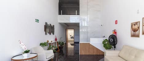Un área de recepción moderna con un sofá blanco, una mesita redonda con un jarrón de flores y un mostrador de recepción.
