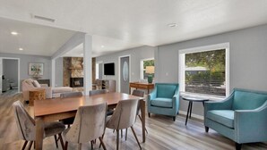 Amplia sala de estar con una mesa de comedor de madera, asientos cómodos, una pared de acento de piedra y un gran ventanal con persianas.