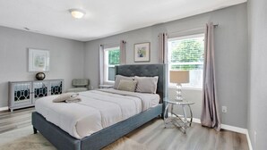 Un dormitorio con cama, mesitas de noche, lámpara y ventana con cortinas.