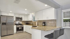 Cocina moderna con armarios blancos, electrodomésticos de acero inoxidable, encimera de granito y una zona de bar con un taburete.