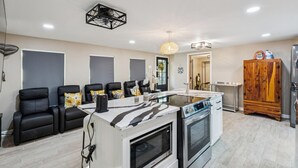 A modern kitchen with a central island, black leather chairs, a wooden cabinet, and a ceiling fan.