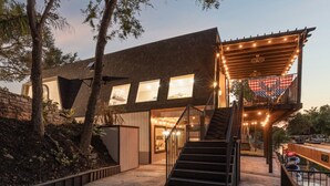 A modern house with a wooden deck, a staircase, and a balcony with string lights.