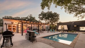 A backyard with a pool, outdoor seating, a grill, and a small bar area.