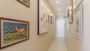 Un pasillo con obras de arte enmarcadas en las paredes, suelo de baldosas y una puerta al final.