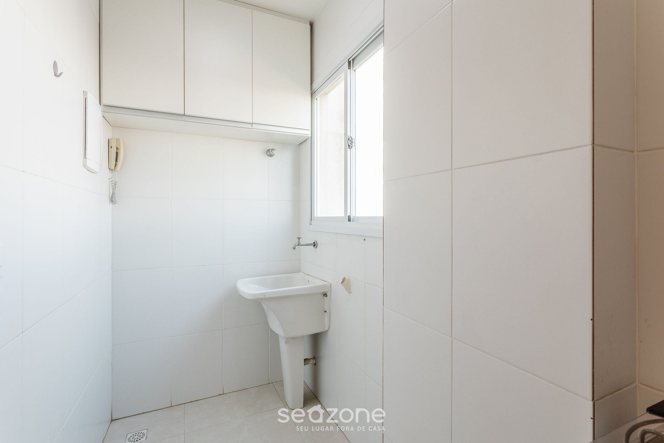 A small, white bathroom with a single sink, a toilet, and a window.