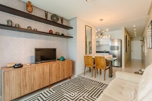 A modern living room with a TV, wooden cabinet, and dining area. - Charming Apt Just 450m From the Beach Emm0202 (Guarapari)