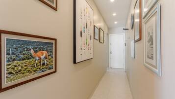 A hallway with framed artwork on the walls, a tiled floor, and a door at the end.