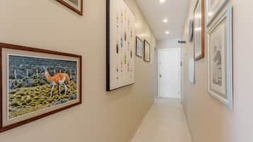 A hallway with framed artwork on the walls, a tiled floor, and a door at the end.