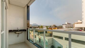 A balcony with a view of a cityscape, a small sink, and a glass railing.