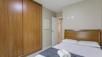 A bedroom with a wooden wardrobe, a bed with white linens, and a grey blanket.
