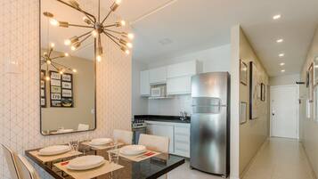 Una cocina moderna con armarios blancos, un refrigerador de acero inoxidable y un comedor con un espejo grande y luces colgantes.
