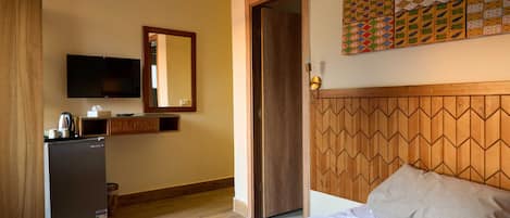 A hotel room with a bed, a television, a small refrigerator, a wooden headboard, and a wall with a geometric patterned artwork.