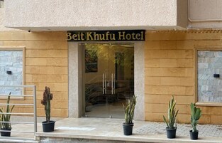 Beit Khufu -hotellin sisäänkäynti, jossa on läpinäkyvä lasiovi, ruukuissa olevia kasveja ja sisäänkäynnin yläpuolella oleva kyltti.