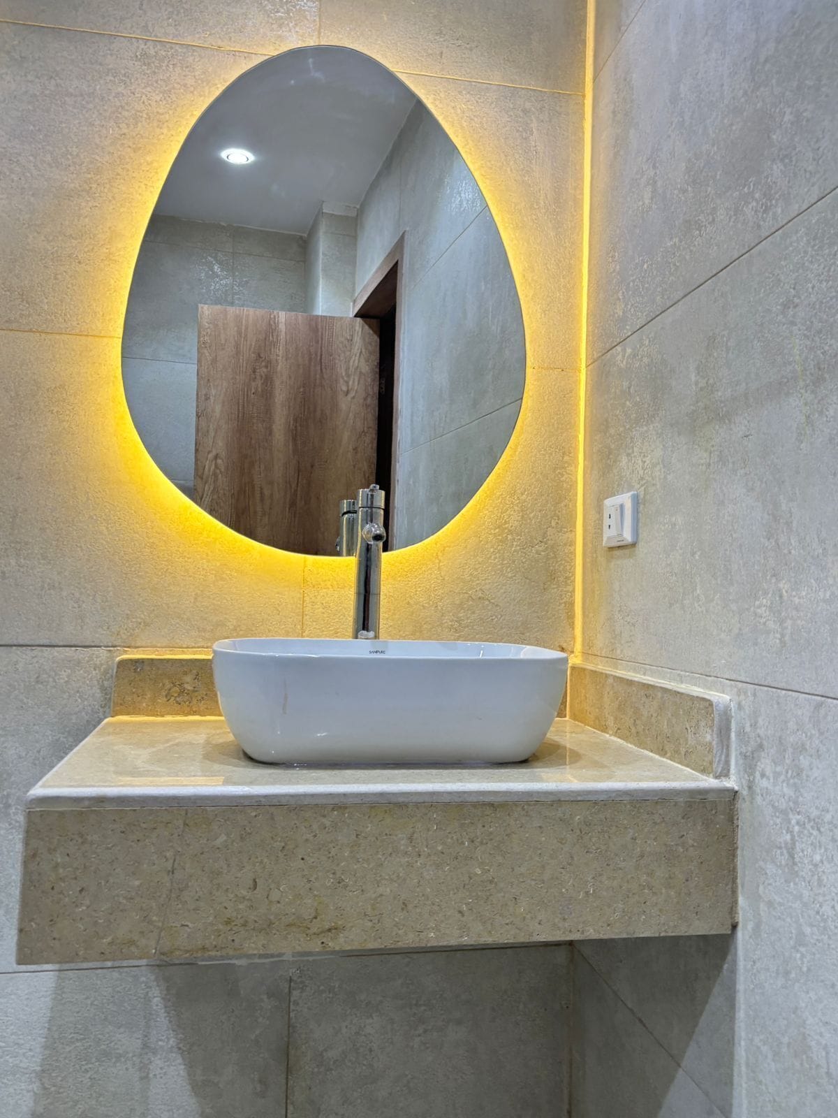 A modern bathroom with a round mirror, a white vessel sink, and a wooden cabinet.