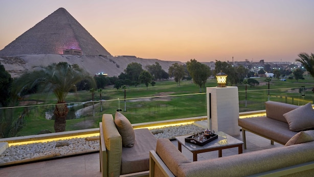 Una terraza con vistas a una pirámide, mobiliario exterior y un campo de golf al fondo.