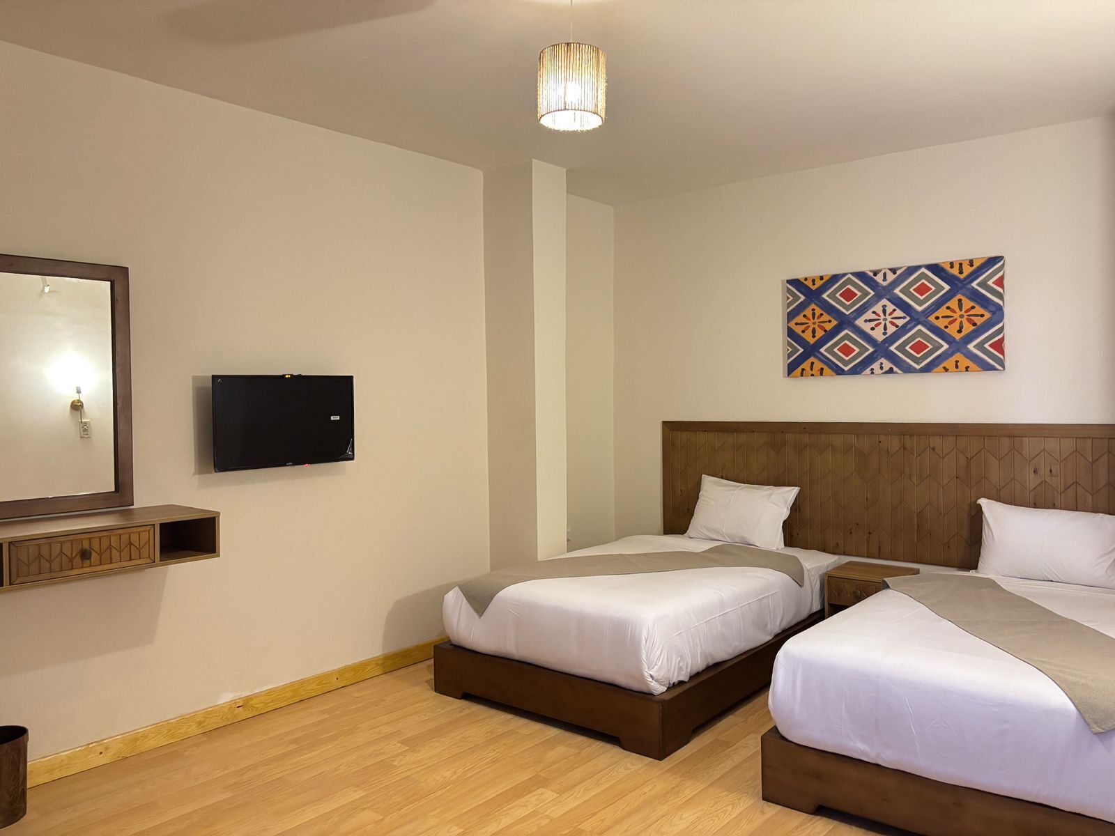 A hotel room with two single beds, a TV mounted on the wall, and a decorative wall hanging.