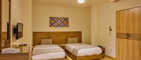 A hotel room with two beds, a wooden wardrobe, a mirror, a bedside table, a TV, and a decorative wall piece.