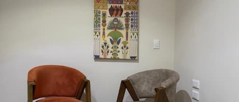 Une pièce avec deux chaises, une œuvre d’art accrochée au mur et un interrupteur.