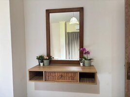 A wall-mounted shelf with a mirror above it, flanked by two potted plants.
