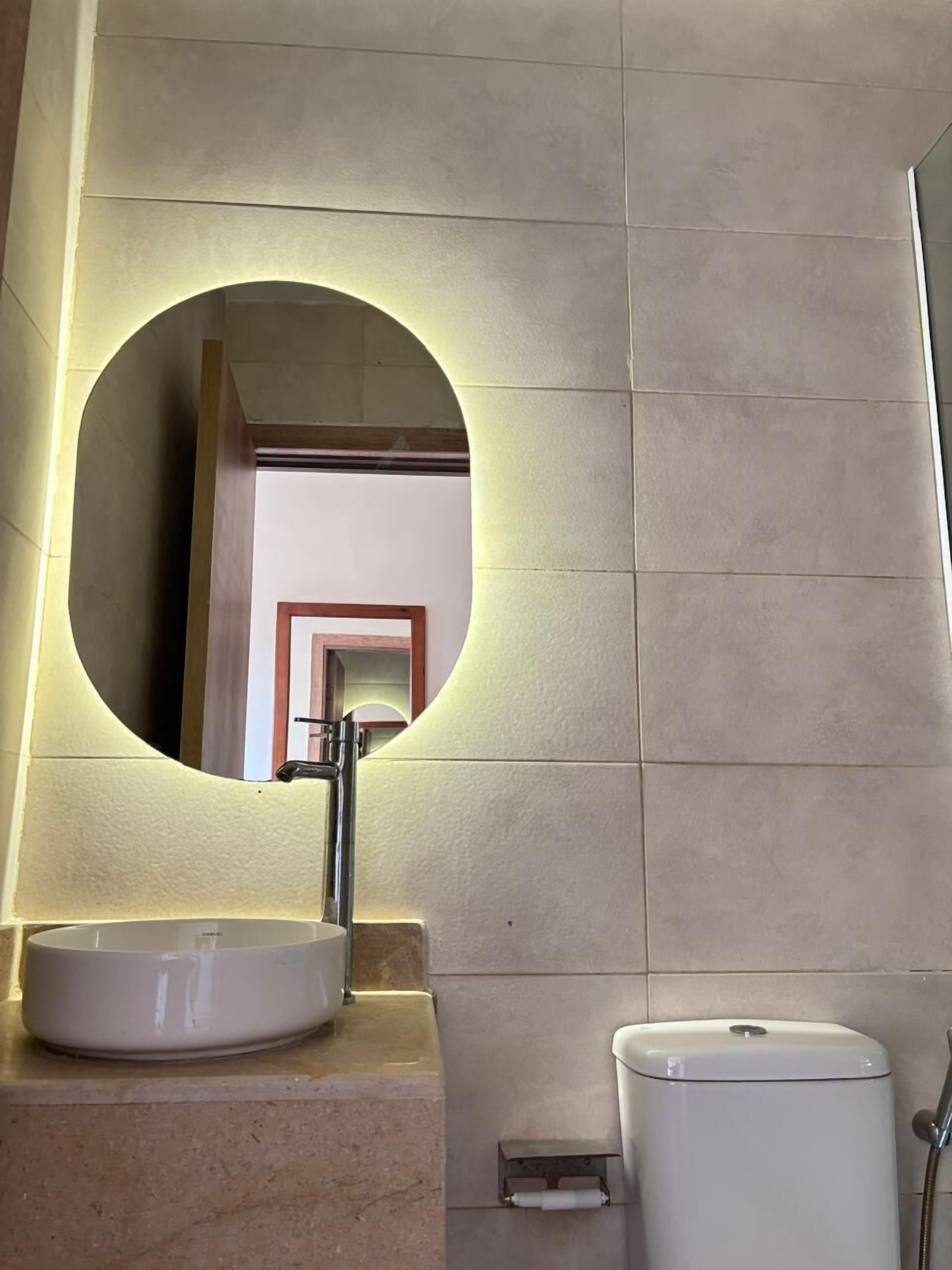A bathroom with a round mirror, a sink, and a toilet.