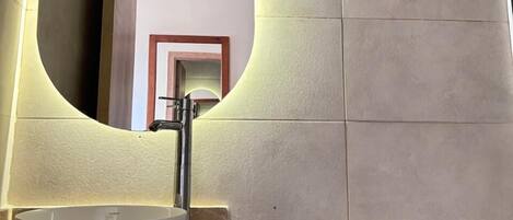 Une salle de bain avec un miroir rond, un lavabo et des toilettes.