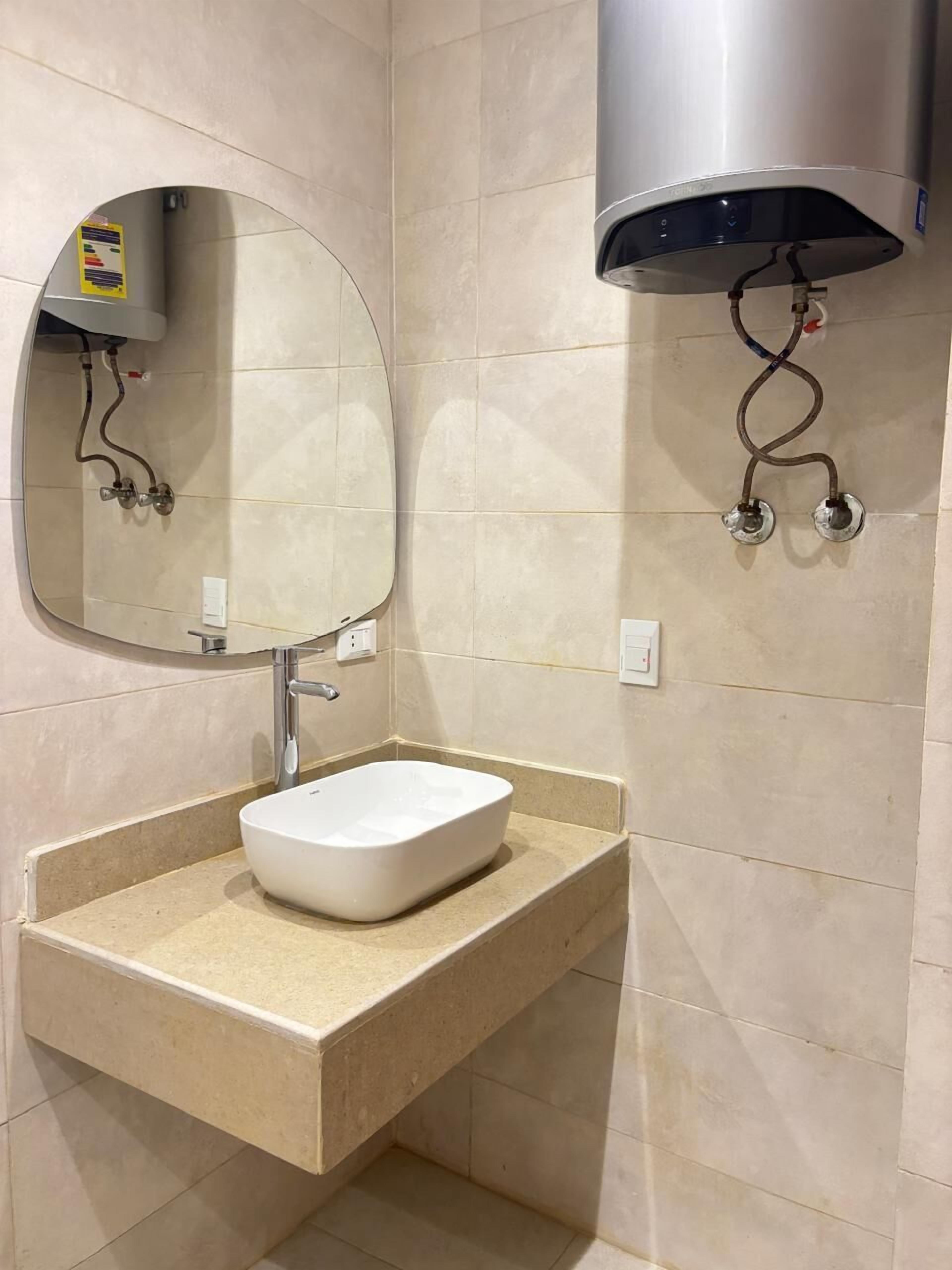 A bathroom with a white sink, a round mirror, and a wall-mounted heater.