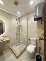 A modern bathroom with a glass-enclosed shower, a toilet, and a sink with a marble countertop.