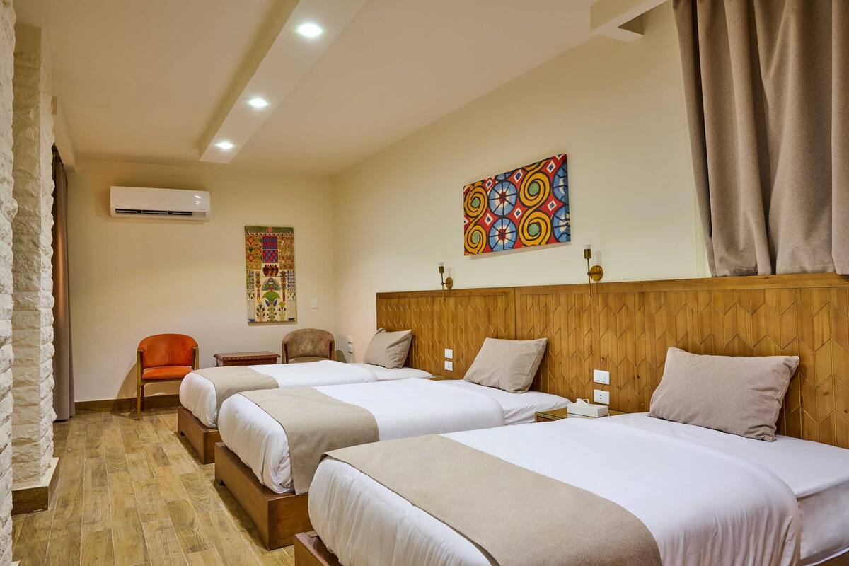 Habitación de hotel con tres camas, cabecera de madera, un adorno en la pared y pared de piedra.