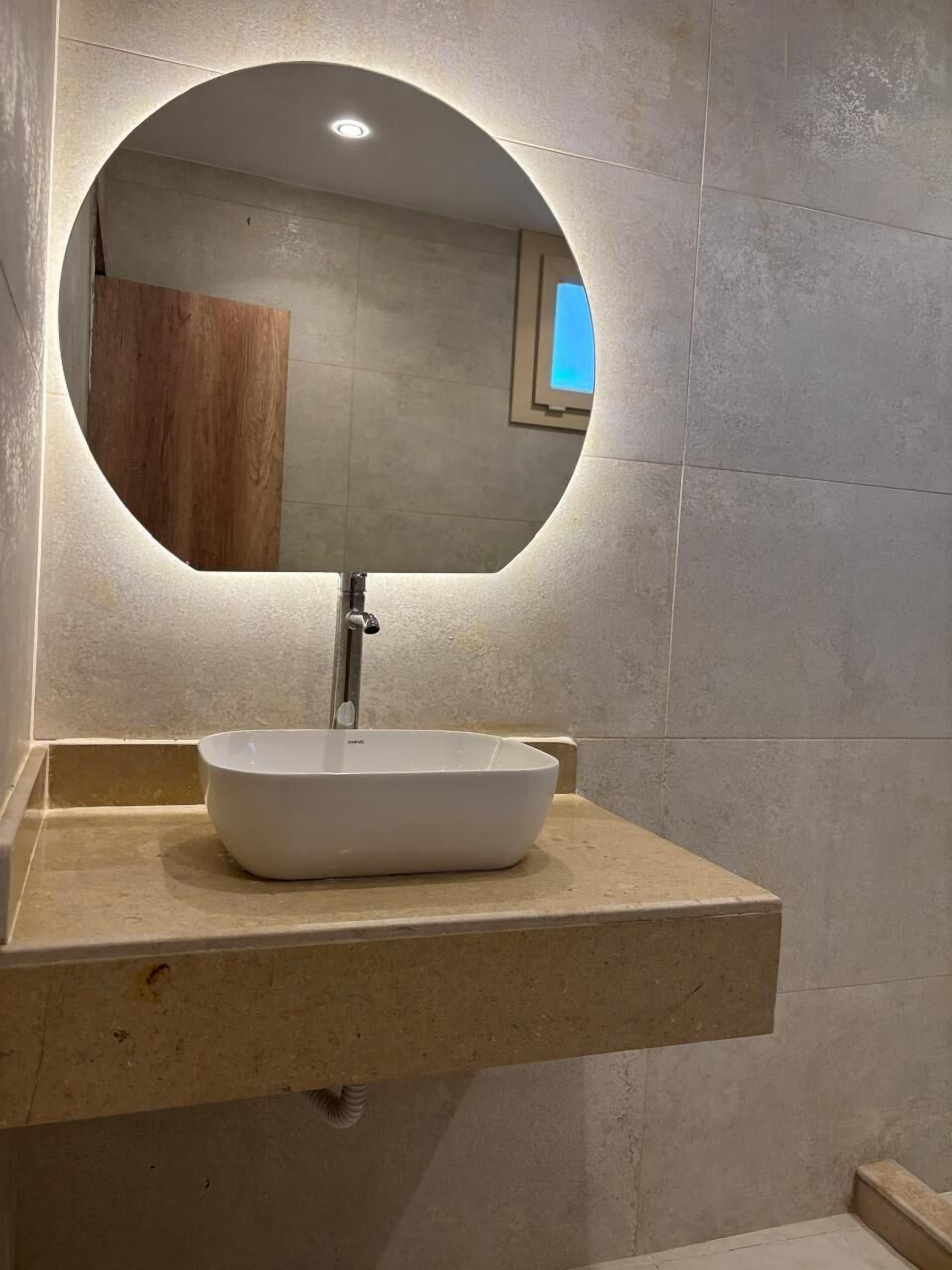 Un baño con un espejo redondo, un lavabo blanco y un armario de madera.
